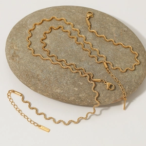 Golden stainless steel wavy twisted chain necklace displayed on a natural grey stone
