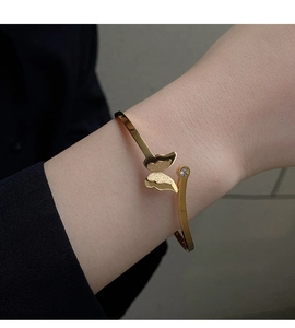 Detail of a 18k gold butterfly open bangle with matte finish and a small diamond accent