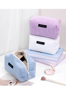 Close-up of three corduroy makeup bags in purple, white, and blue with vertical textures
