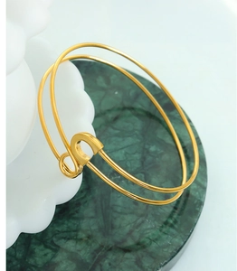 Detail view of a gold safety pin bangle on green marble with ceramic decor