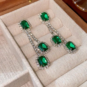 Macro detail of emerald-green square earrings with diamonds on a beige jewelry box