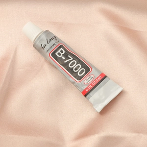 Macro shot of B-7000 clear universal glue tube for jewelry on soft pink fabric