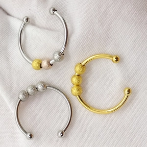 Close-up of three adjustable stainless steel rings with rotating beads on white fabric