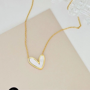 Detail of a gold heart pendant necklace with white mother of pearl inlay on a card