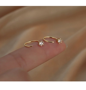 Macro shot of minimalist gold C-shaped earrings with six-prong cubic zirconia setting