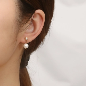 Detail of gold C-shaped earring with sparkling zircon and white round pearl on ear