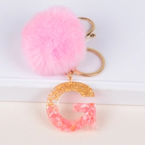 Macro detail of a pink faux fur pompom and resin letter G charm with gold leaf