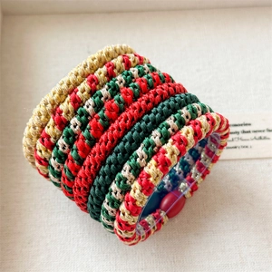 Close-up of red, green and gold woven Christmas elastic hair ties on a soft cream base