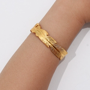 Macro detail of 18K gold plated feather cuff bracelet with intricate leaf engraving