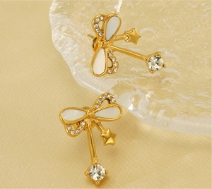 Detail of gold bow earrings with crystal accents and star charms on glass tray