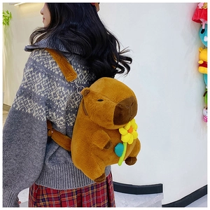 Brown plush capybara backpack accessory with a yellow flower on a model's back