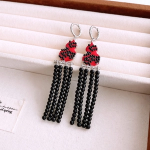 Detail of red gourd earrings with black beaded tassels on a beige jewelry tray