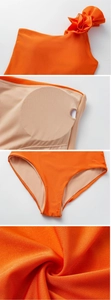 Detail of orange one-shoulder swimsuit featuring 3D floral accents and removable chest pads