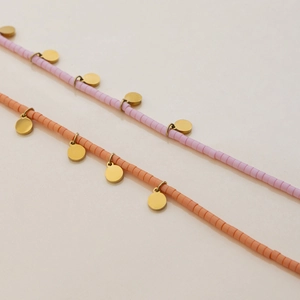 Detail of pink and orange beaded necklaces with small round gold fish pendants