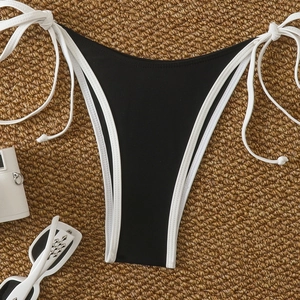 Detail of black thong bikini bottoms with white trim and side-ties on a straw mat