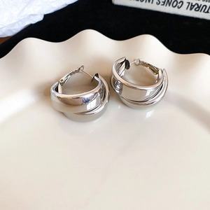 Macro shot of silver metal layered wide hoop earrings on a decorative cream ceramic tray