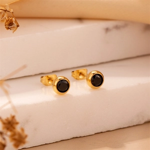 Classic round gold bezel earrings with black zircon displayed on a marble stand