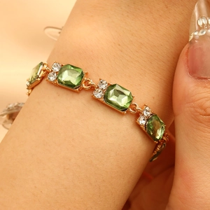 Dettaglio di bracciale dorato con pietre quadrate verde smeraldo e punti luce