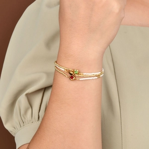 Three-layer gold bead bracelet with red and green zircon charms on a woman's wrist