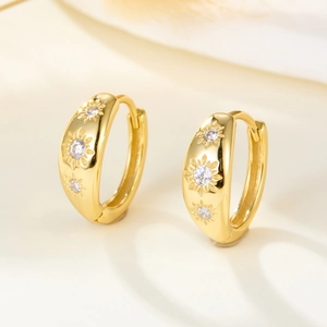 Detail of wide gold huggie earrings with starburst engraving and cubic zirconia