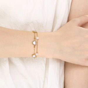 Double-layered gold stainless steel heart and pearl bracelet worn on a model wrist