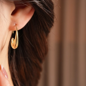 Close-up of minimalist 14k gold plated oval drop earring worn by a model in soft light