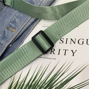 Detail of adjustable green nylon strap with black buckle on a denim jacket background