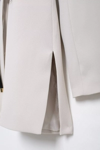 Detailed close-up showing the textured fabric and hem slit of a beige women's suit jacket