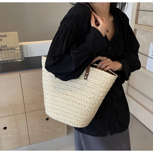 Close-up of woven straw tote bag texture with brown leather strap and contrast stitching
