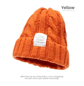Detailed cable knit pattern on orange beanie featuring a white rectangular woven label