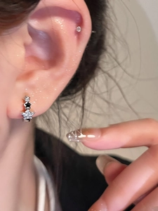 Primer plano de aretes de aro con estrellas, circonita y esmalte negro en la oreja de una modelo