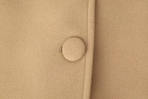 Close-up of camel wool coat fabric with detailed texture and a matching covered button