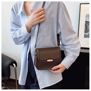 Close-up of a vintage dark brown leather crossbody bag with a gold buckle worn on a shoulder