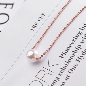 Elegant rose gold titanium steel necklace with a round white pearl pendant on book background