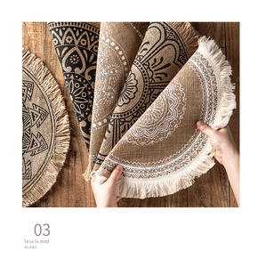 Detail showing hand holding a round jute placemat with mandala pattern and tassel fringe