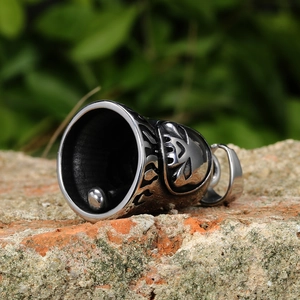 Close-up of a vintage steel skull bell pendant with aged finish on a stone surface