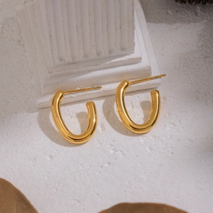 Minimalist U-shaped gold plated stainless steel earrings on white textured background
