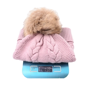 Pink knit beanie with faux fur pom pom and cable pattern on digital scale weighing 138g