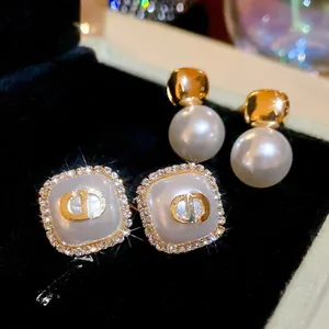 Detailed macro view of square gold CD logo earrings with pearl and crystal halo on black velvet