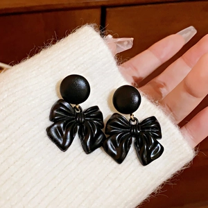 Detailed view of elegant black bow earrings pinned on a white knitted sweater cuff