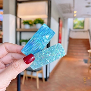 Detail of two blue holographic and glitter rectangular hair clips held by hand