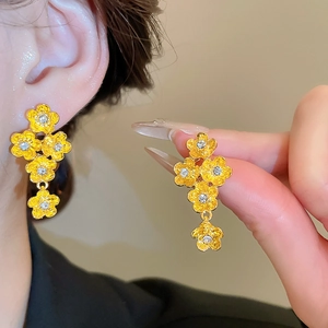 Detailed close-up of golden floral drop earrings with white crystals and matte finish texture