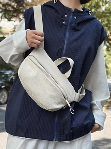 Minimalist beige nylon crossbody chest bag with adjustable strap worn by a model