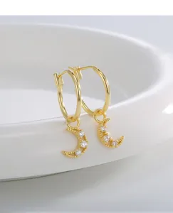 Detail of gold moon pendant earrings with zircon stones on a white ceramic plate