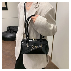 Detail of black patent leather bowling bag with gold hardware worn with beige blazer