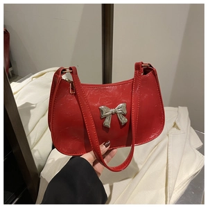 Detailed view of glossy red patent leather handbag featuring a metallic silver bow