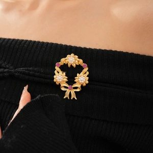 Elegant gold flower wreath brooch with pearls and pink gems on a black sweater