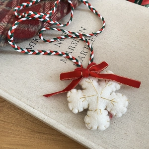 Detailed close-up of white wool felt snowflake pendant with red velvet bow on a woven cord