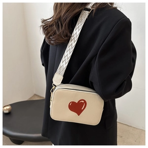 Detail of beige crossbody bag with red heart pattern and wide geometric woven strap