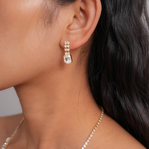 Close-up of gold earrings with square-cut crystal and sparkling stones on a model